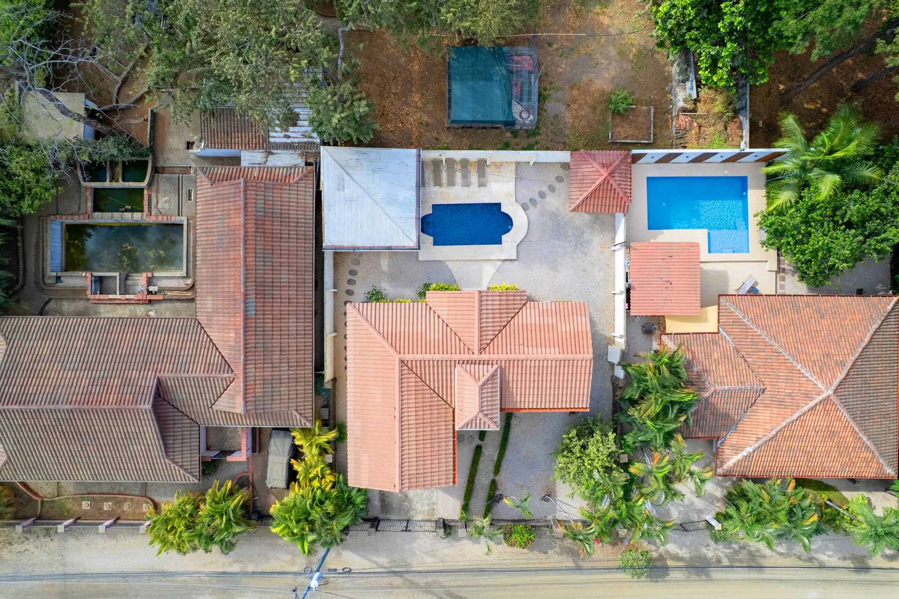 An aerial view shows a swimming pool and tiled-roof buildings among trees.
