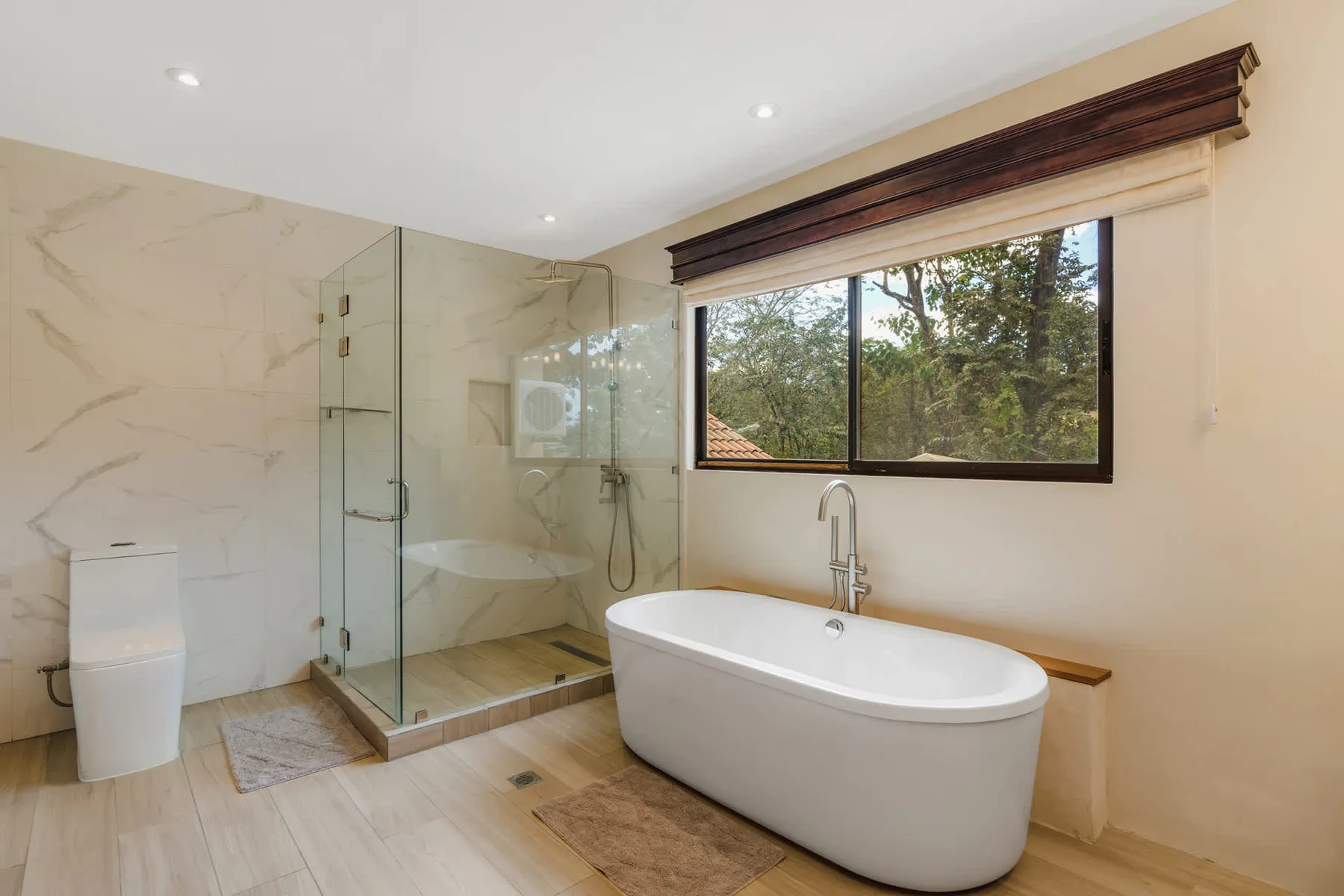 A bright bathroom features a freestanding tub beside a glass shower and large window.