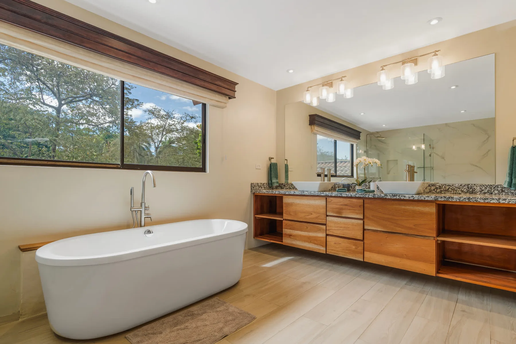 A bright bathroom features a freestanding bathtub beneath a large window.