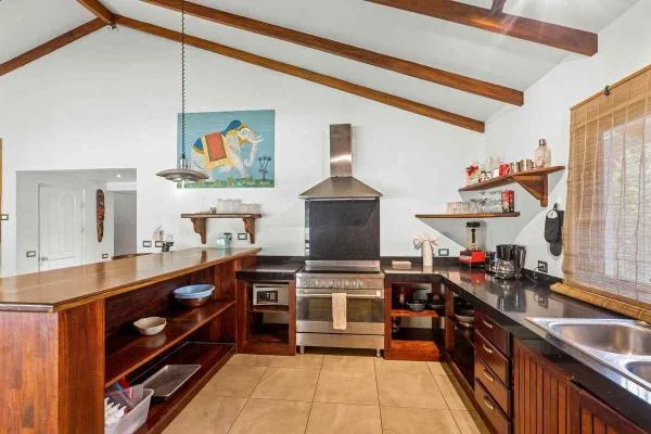 Cocina con vigas de madera a la vista, una estufa central y encimeras oscuras alrededor de un suelo de baldosas.
