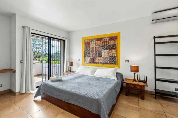 Un dormitorio con una cama grande, arte colorido en la pared, mesitas de noche y puertas corredizas de vidrio hacia un balcón.