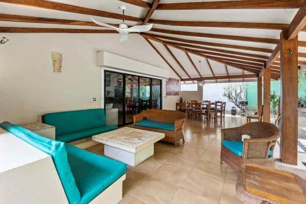 Una amplia sala de estar y comedor tiene asientos turquesa, una mesa baja y vigas de madera expuestas.