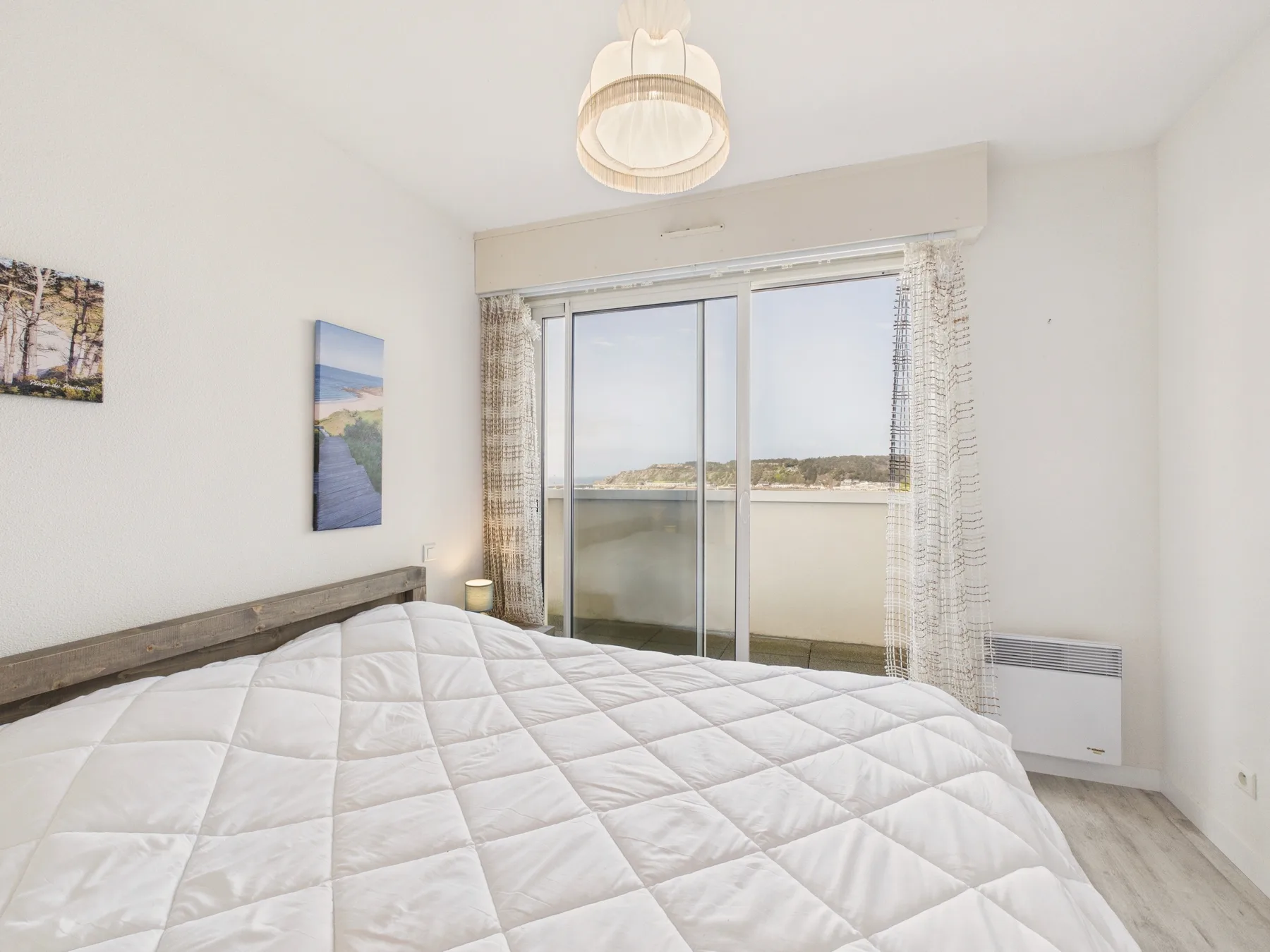 Un dormitorio luminoso con una cama frente a puertas corredizas de vidrio y vistas al agua.