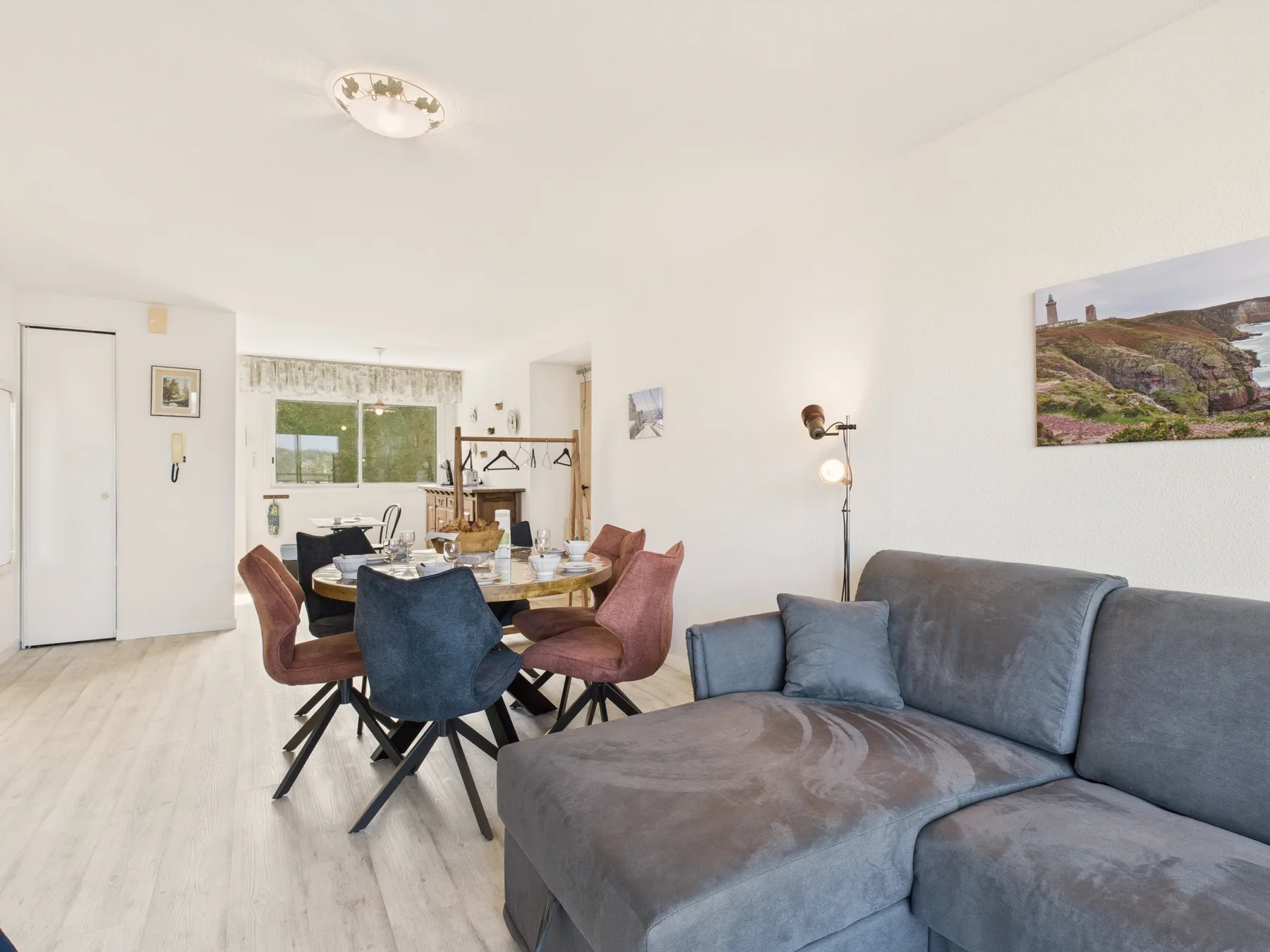Una luminosa sala de estar y comedor con un sofá seccional gris y una mesa rodeada de asientos.