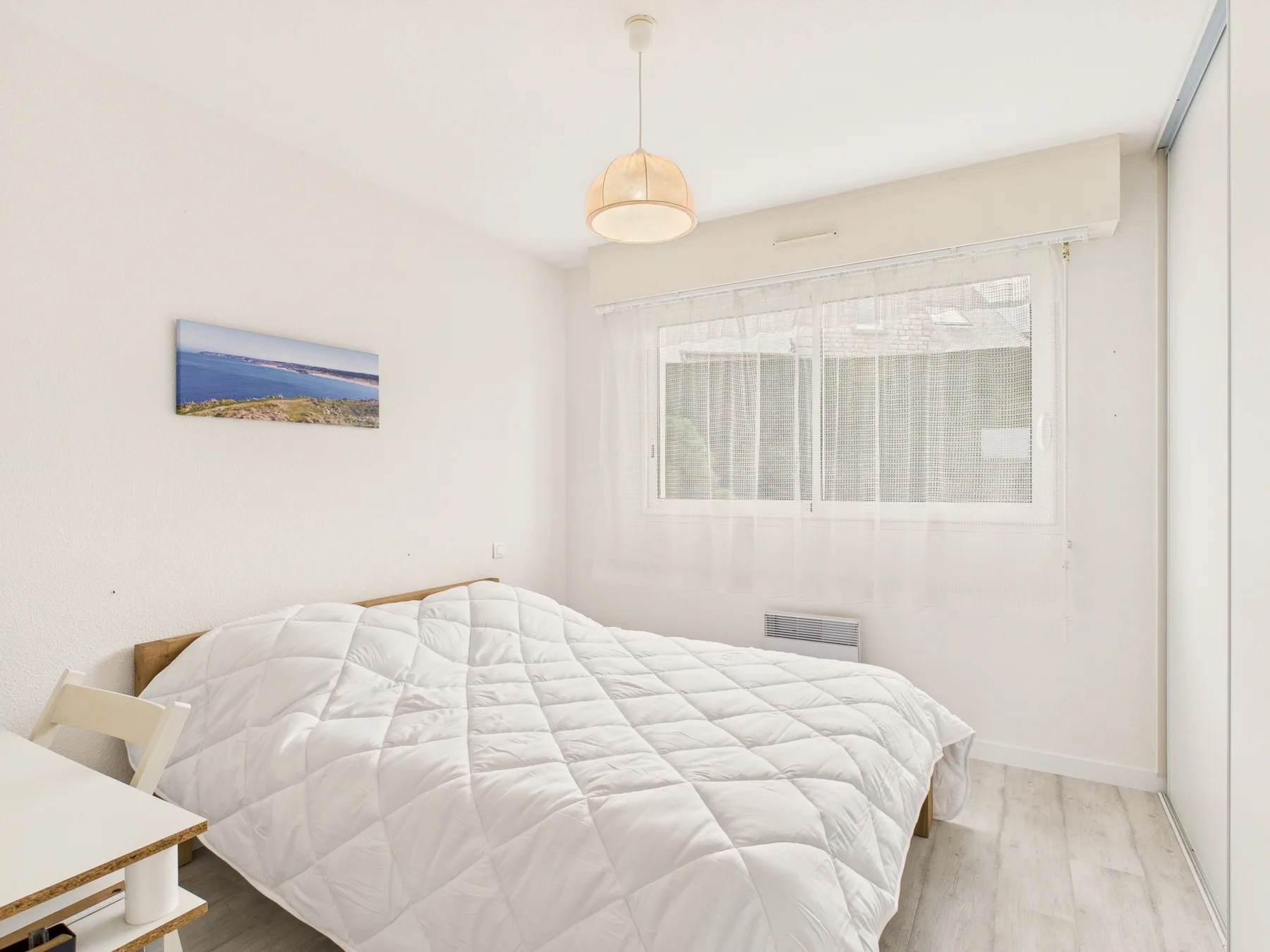 Un dormitorio luminoso con una cama debajo de una ventana grande.