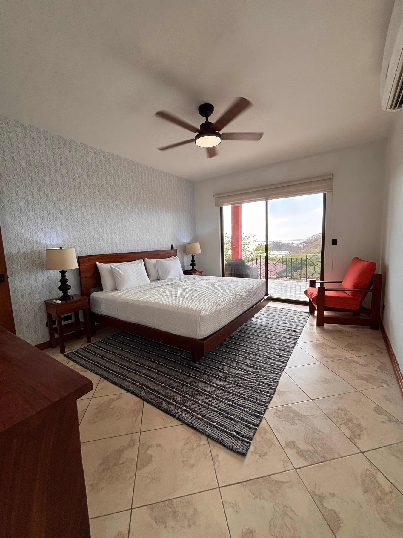 A bedroom with a bed, striped rug, and sliding glass doors opening to a balcony.