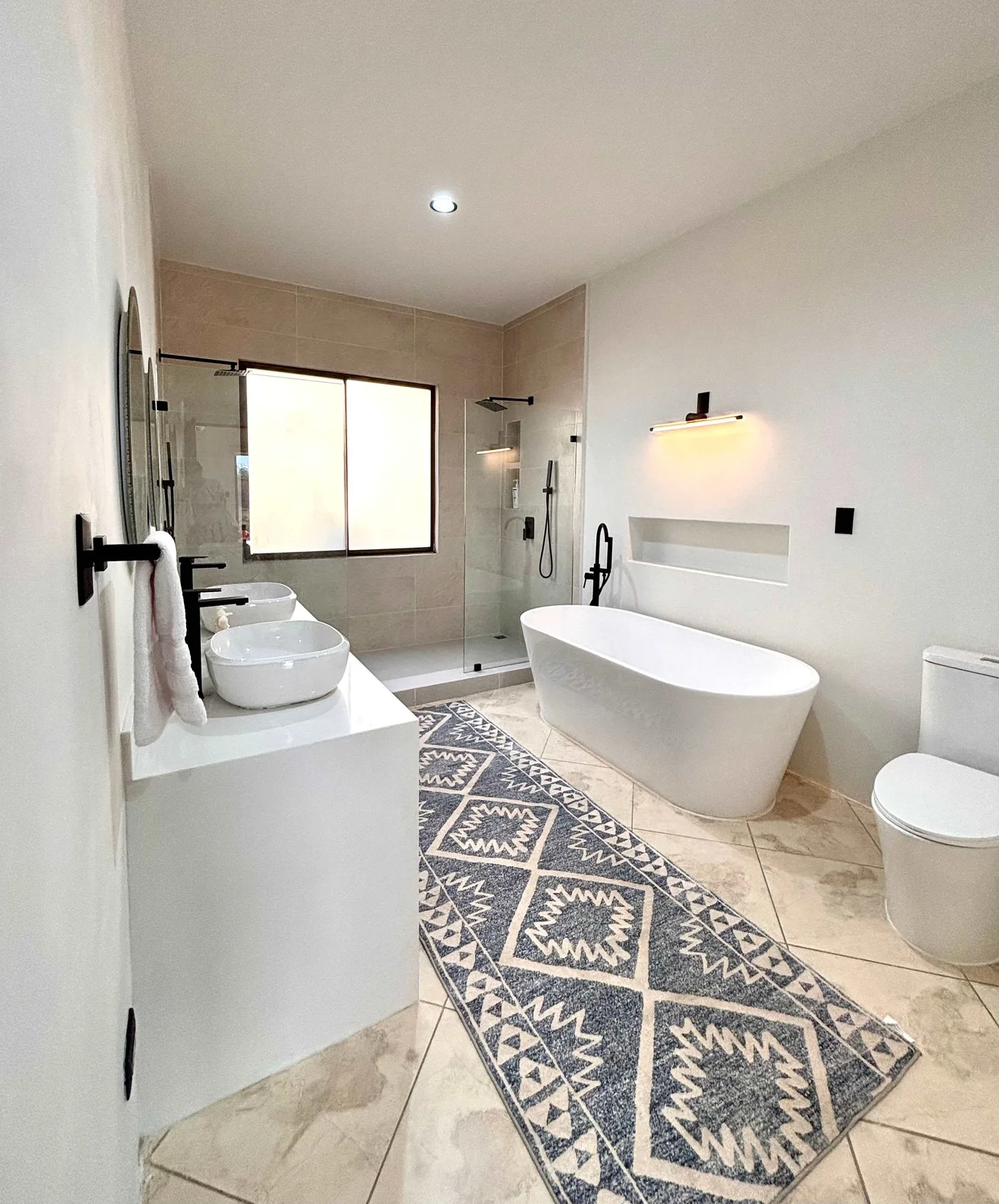 A modern bathroom with a bathtub, glass shower, and patterned floor runner.