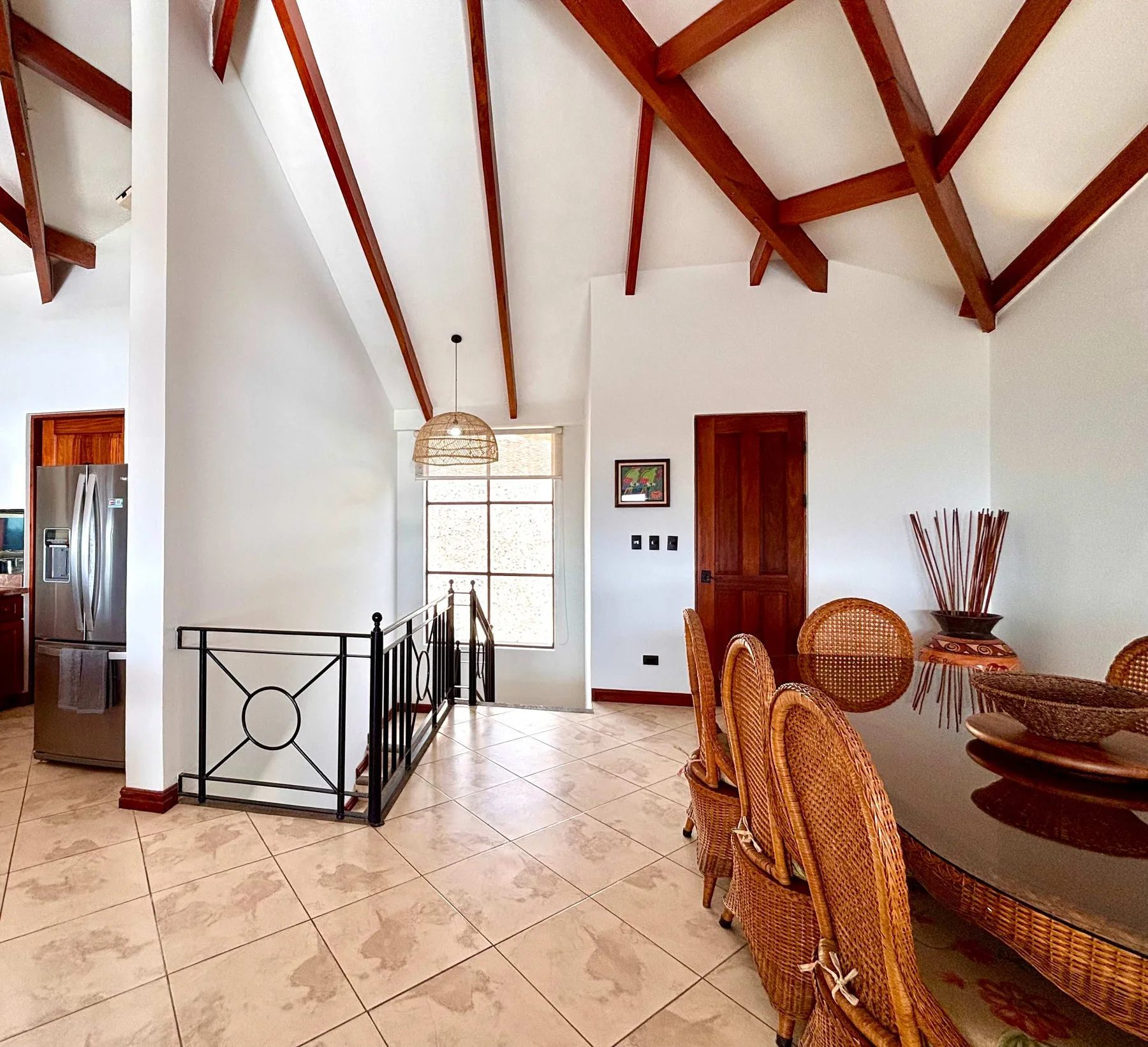A bright dining area with wicker seating beneath exposed wooden ceiling beams.