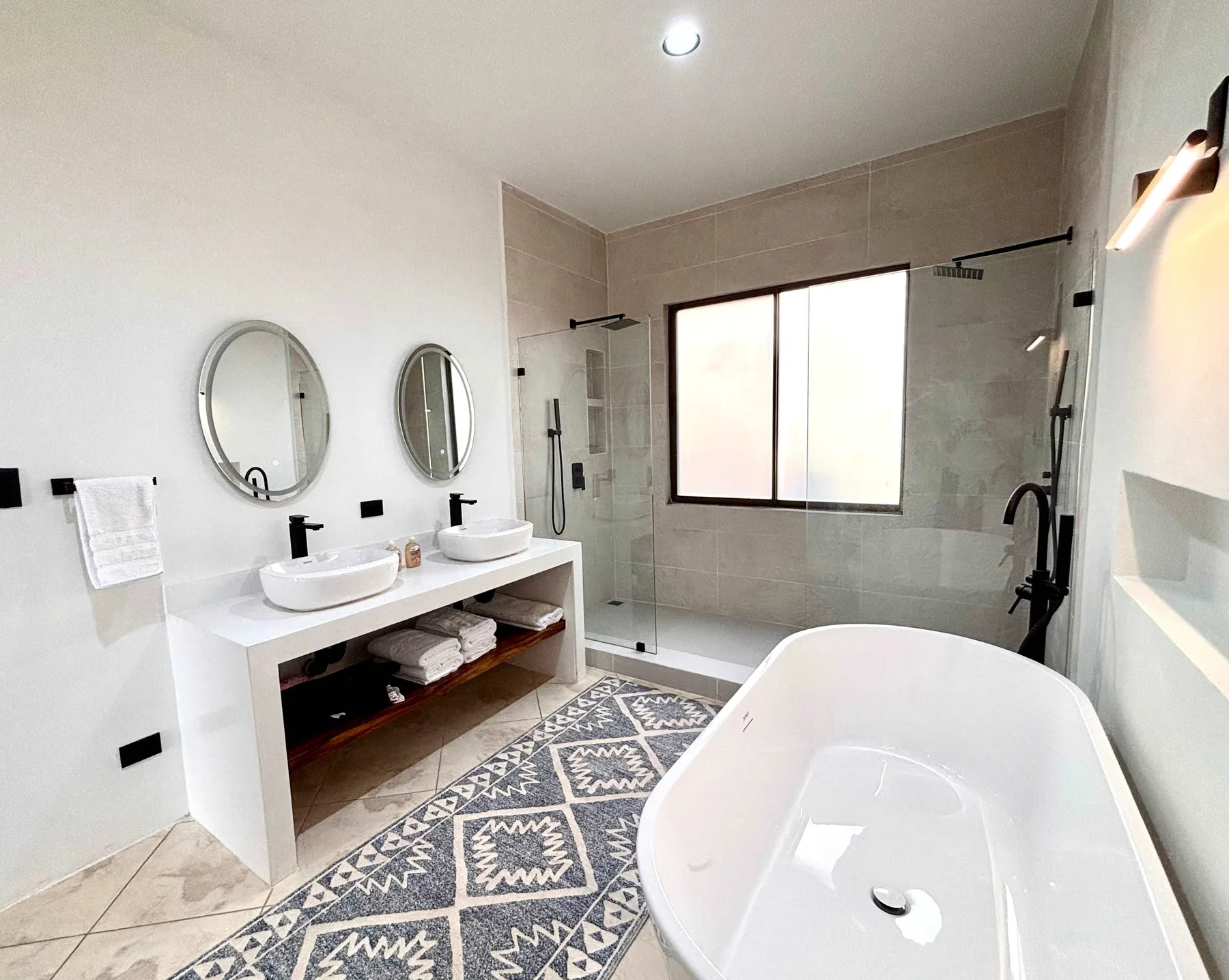A bright bathroom has a bathtub, glass shower, and double vanity.