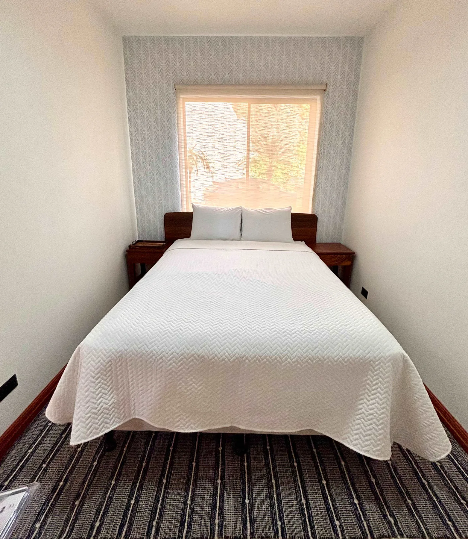 A bedroom with a neatly made bed positioned beneath a bright window.