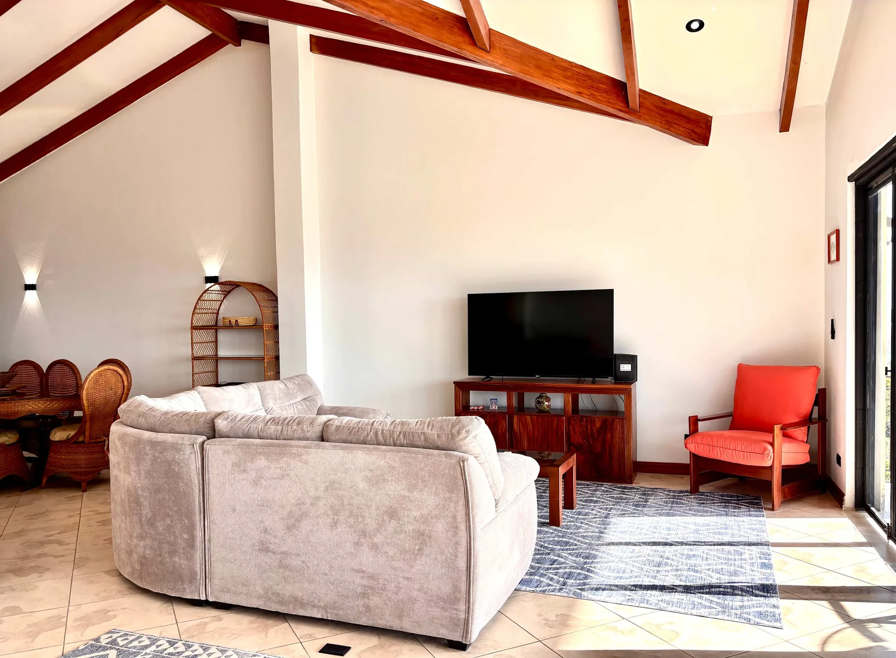 A bright living room with seating, a television, and exposed wooden ceiling beams.