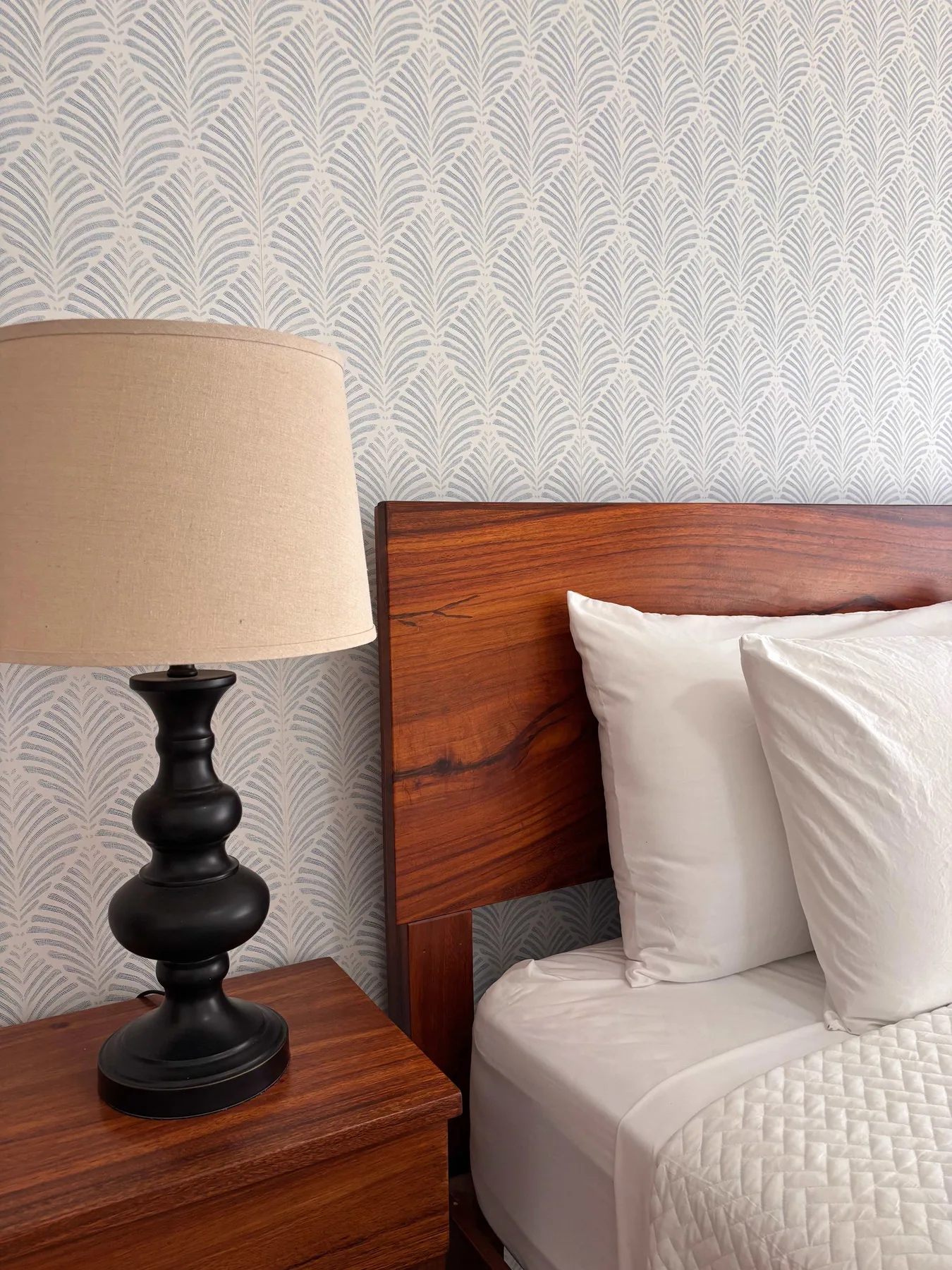A bedroom scene with a bed, white pillows, and a bedside lamp.