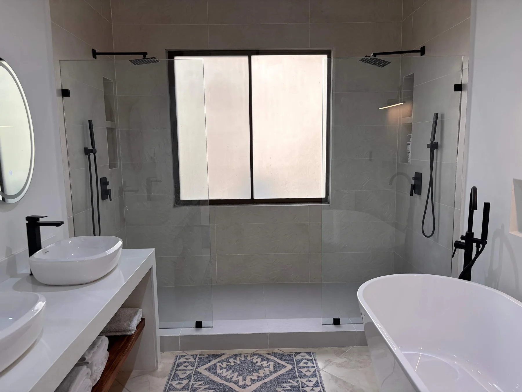 A tiled bathroom with a double sink vanity, shower, and freestanding bathtub.