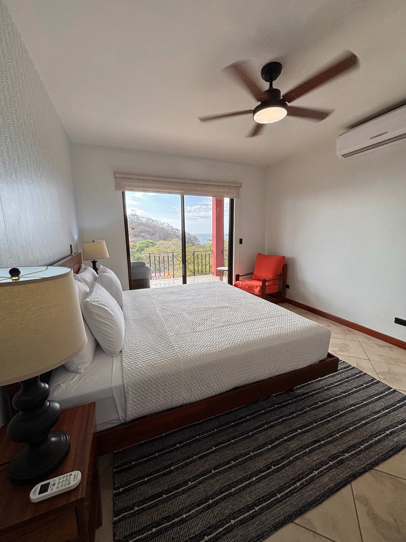 A bedroom with a large bed, a red chair, and sliding glass doors overlooking greenery.