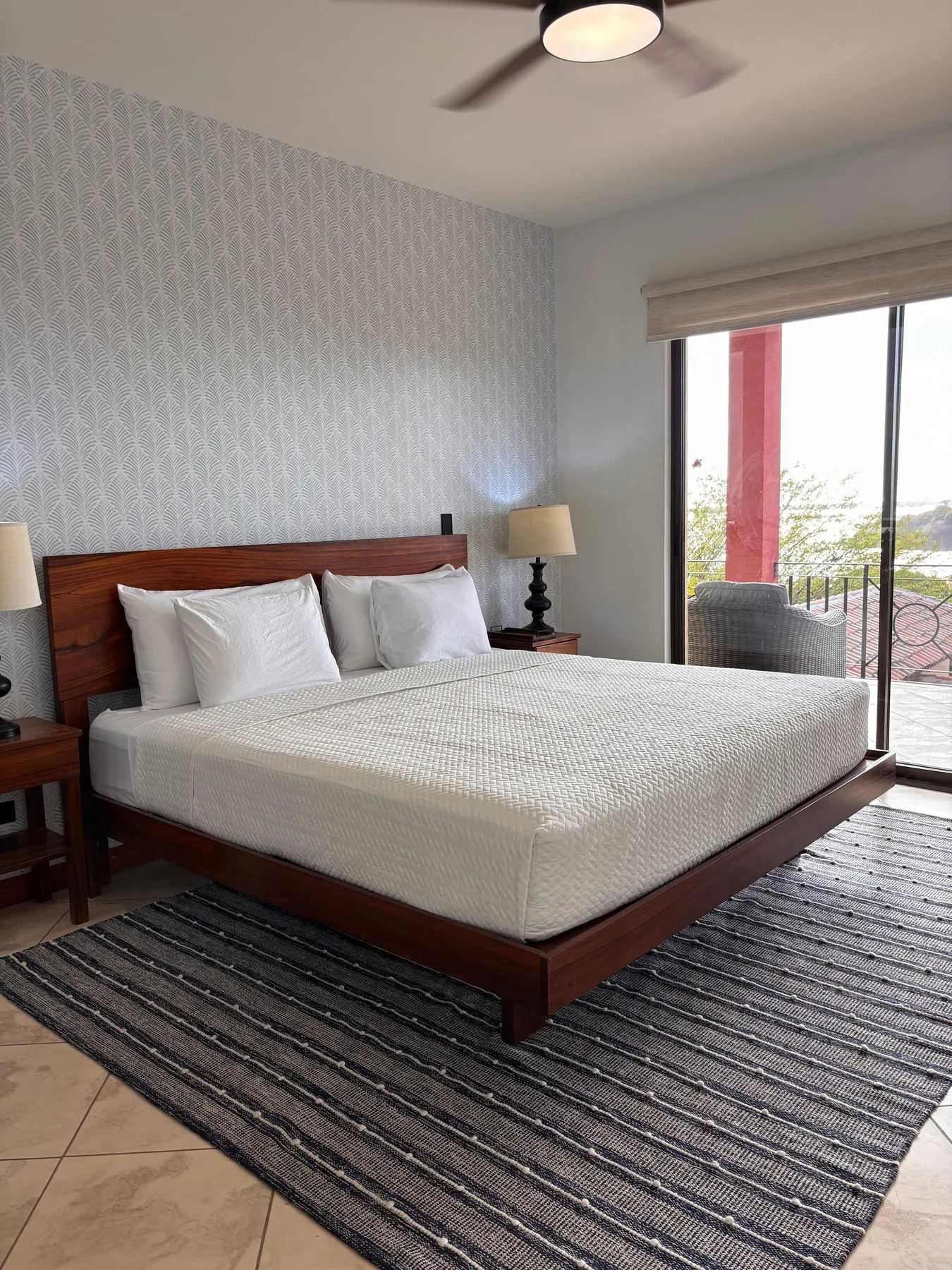 A bedroom with a neatly made bed beside a glass door opening to a balcony.