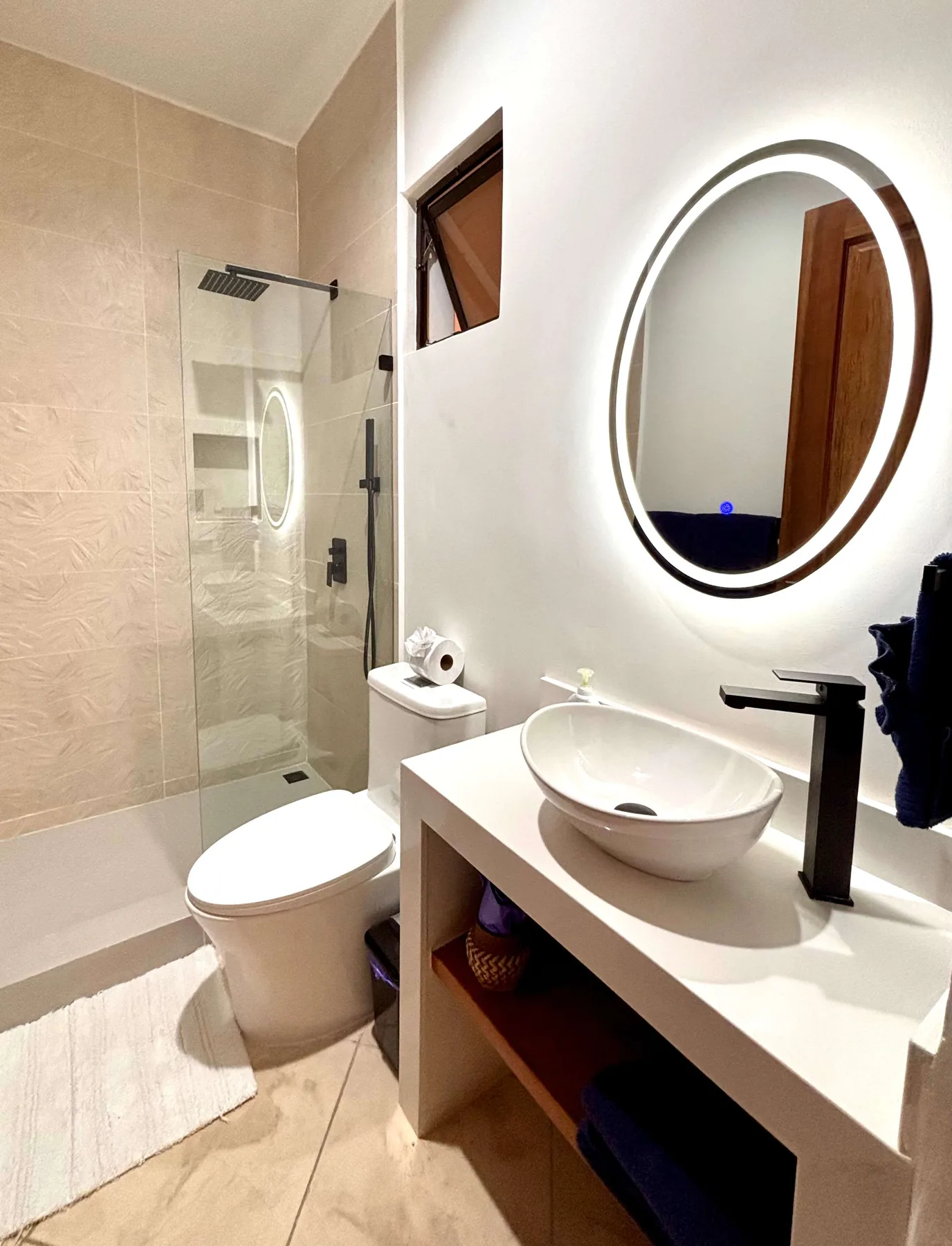 A bathroom with a sink, round mirror, toilet, and glass shower.