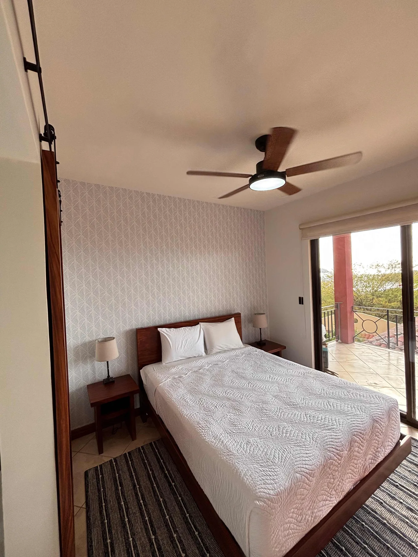 A bedroom with a bed beside a sliding glass door opening onto a balcony.