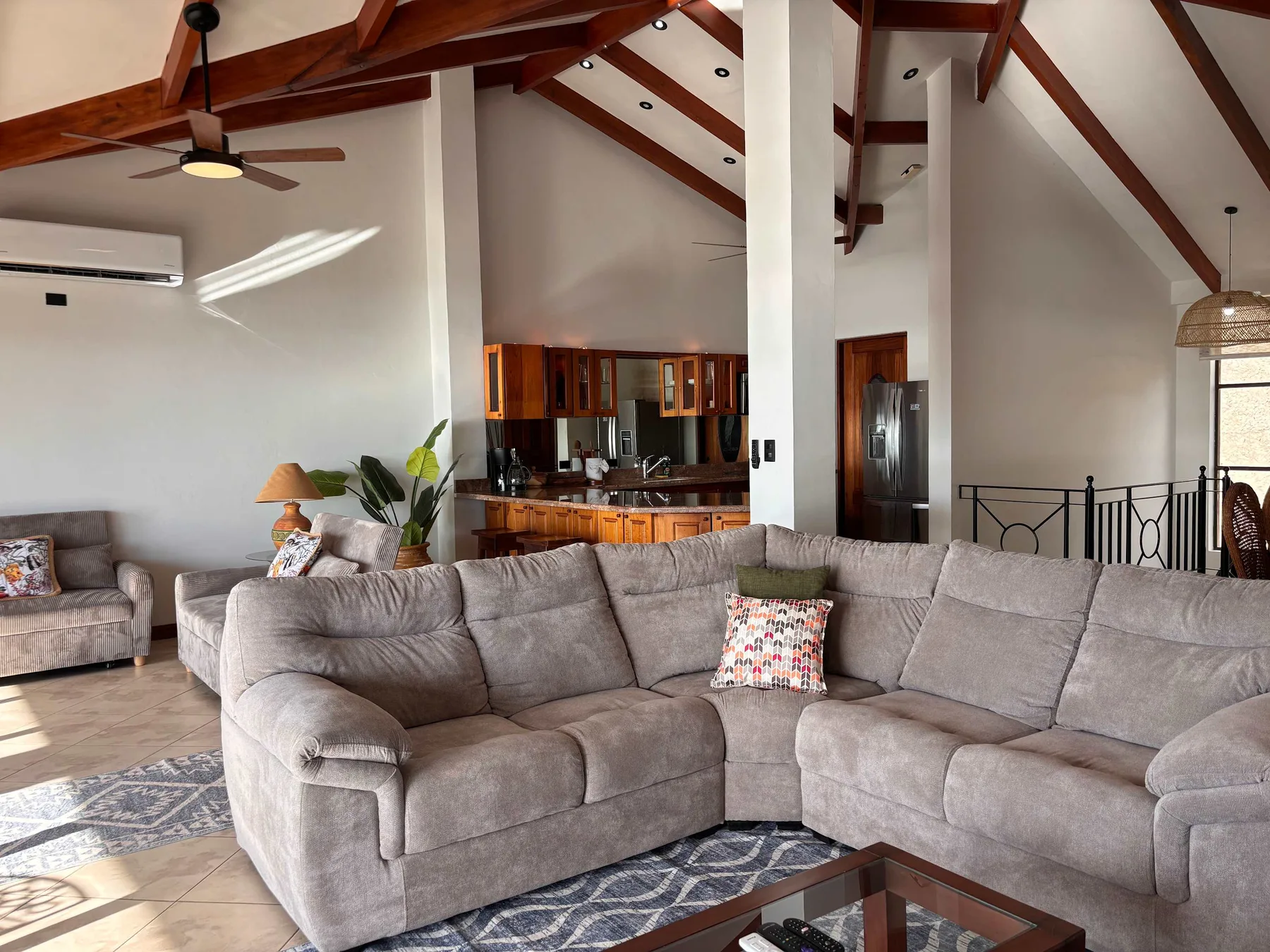 A spacious living room with gray seating and an open kitchen in the background.