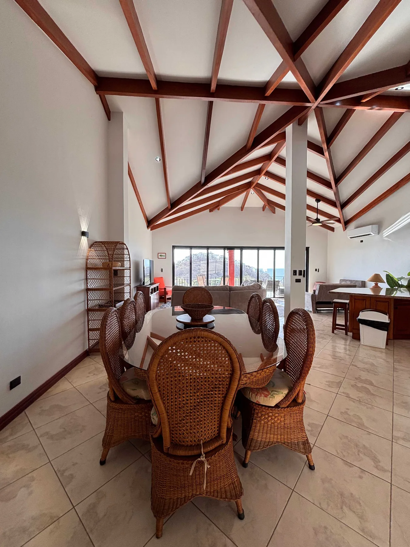 A dining area with a wicker table and chairs beneath exposed wooden ceiling beams.