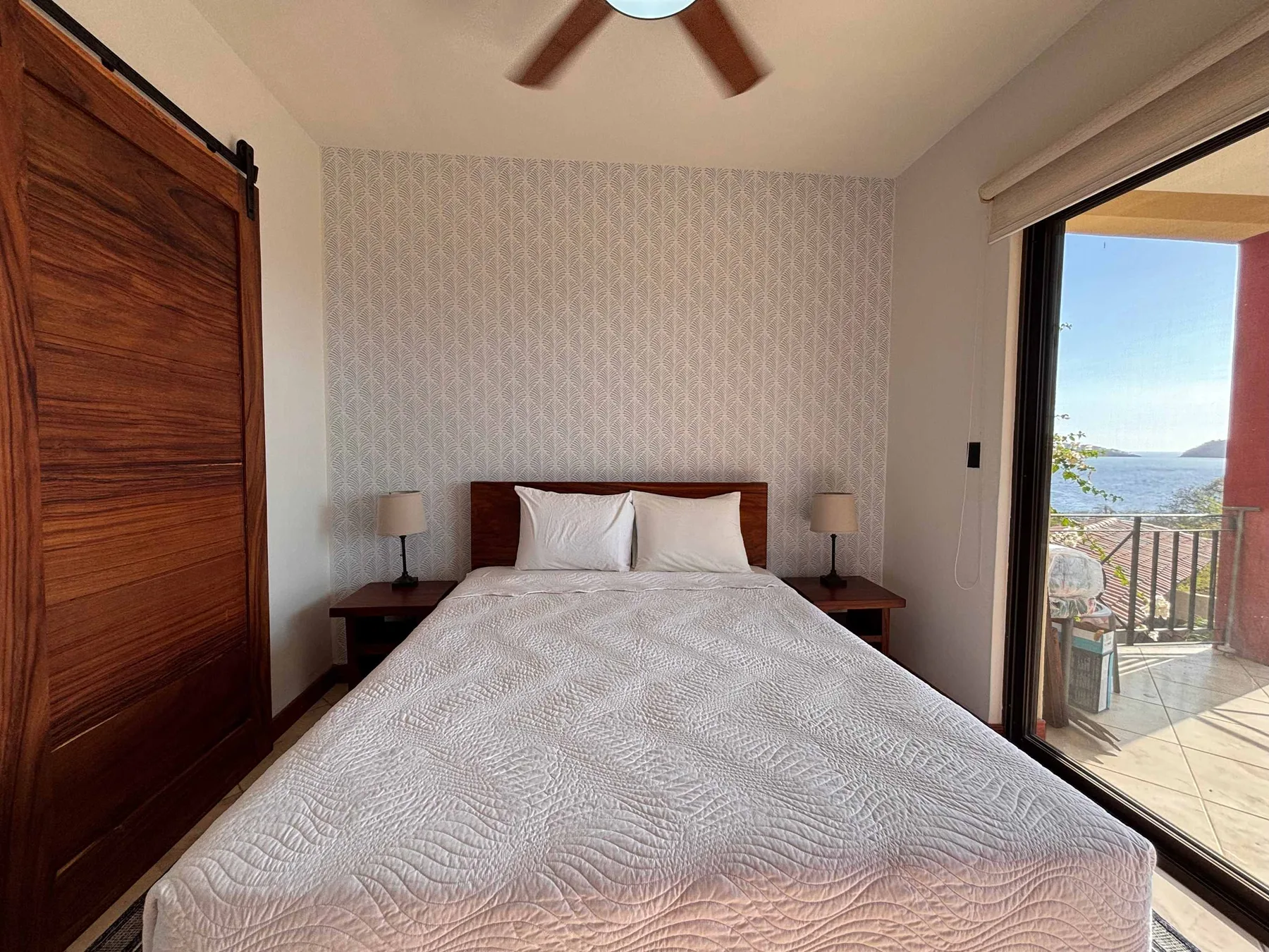 A bedroom with a neatly made bed and a sliding glass door opening to a balcony.