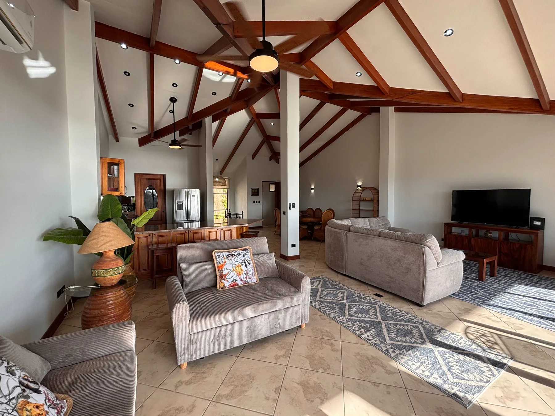 A spacious living room with seating, a television, and exposed wooden ceiling beams.