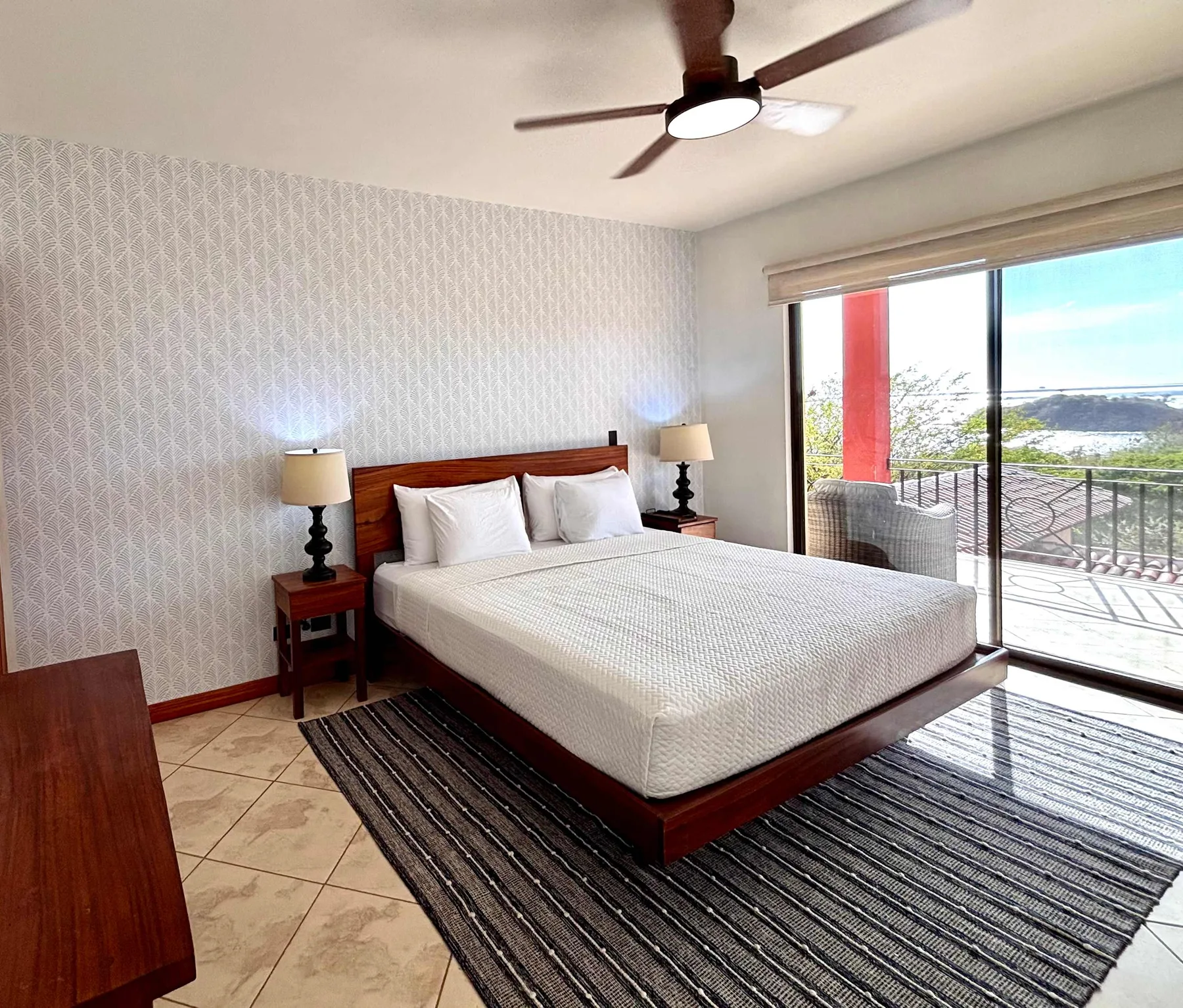 A bedroom with a neatly made bed beside a large sliding glass door.