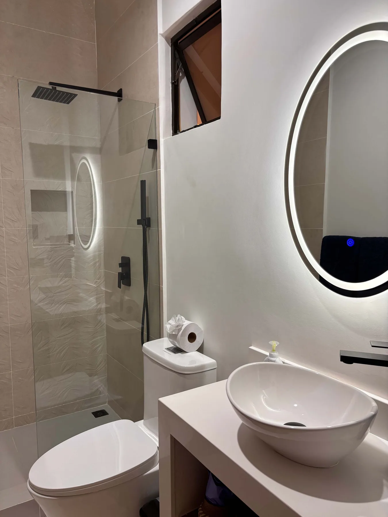 A bathroom with a glass shower, toilet, and sink beneath a round mirror.