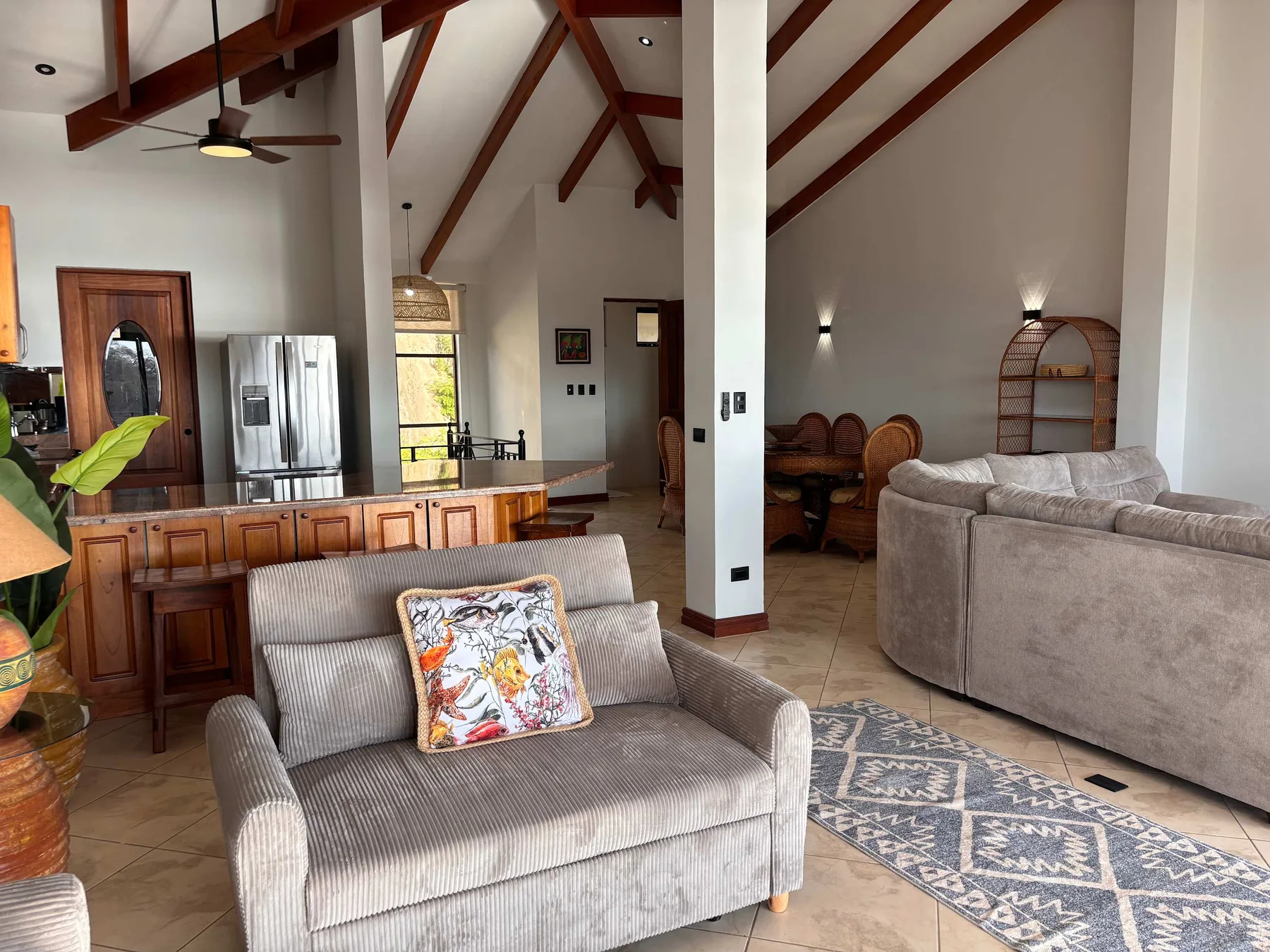 A spacious living room with seating, a kitchen counter, and exposed wooden ceiling beams.