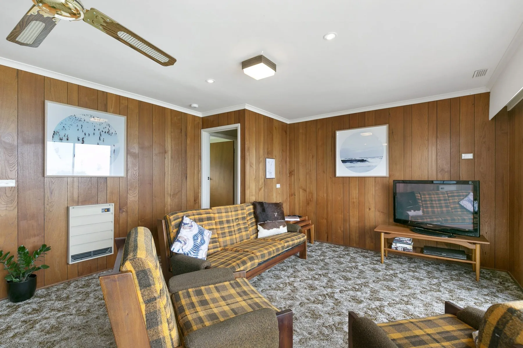 Una sala con paredes de madera, asientos a cuadros, cuadros enmarcados y un televisor.
