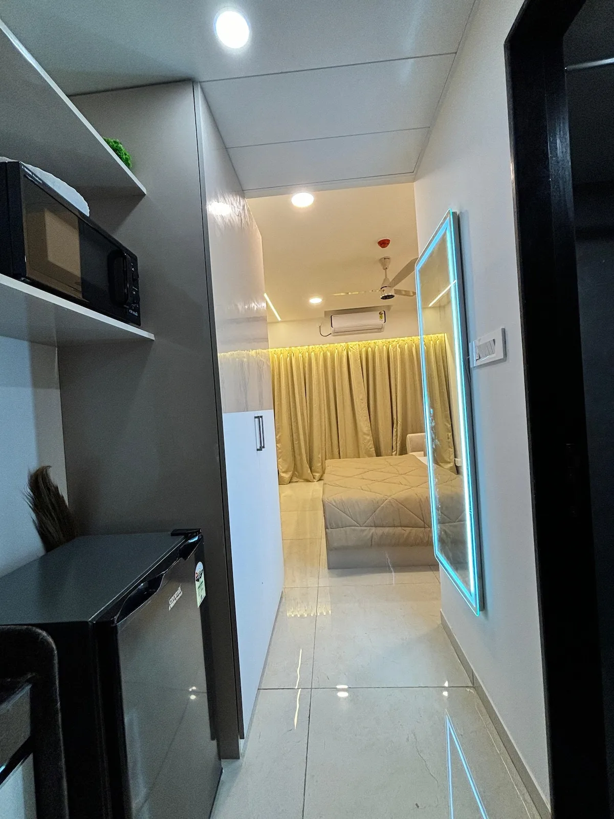 Una habitación compacta con refrigerador, microondas y una cama detrás de las cortinas.
