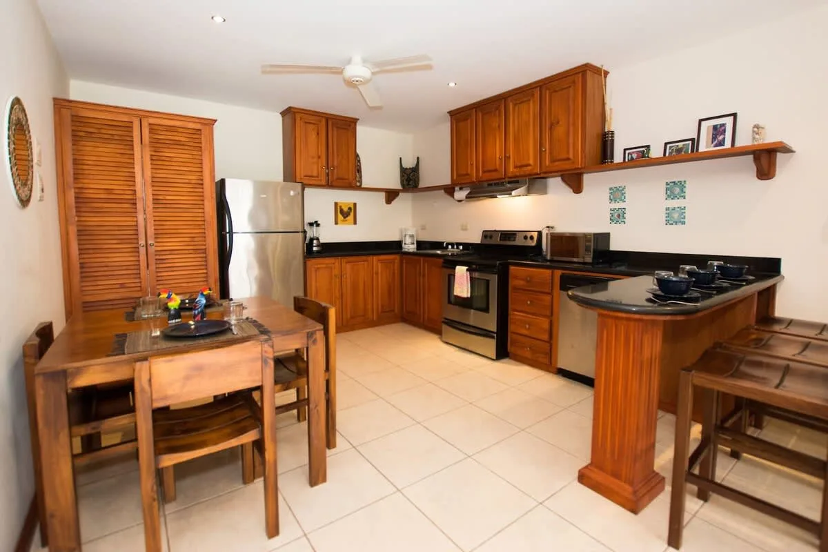Una cocina con gabinetes de madera, electrodomésticos de acero inoxidable y una pequeña mesa de comedor.