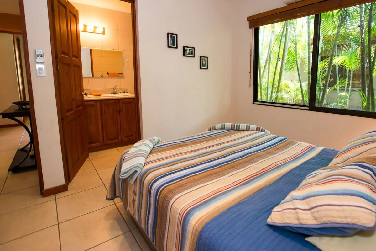 Un dormitorio con una colcha a rayas y una ventana con vistas a la vegetación.
