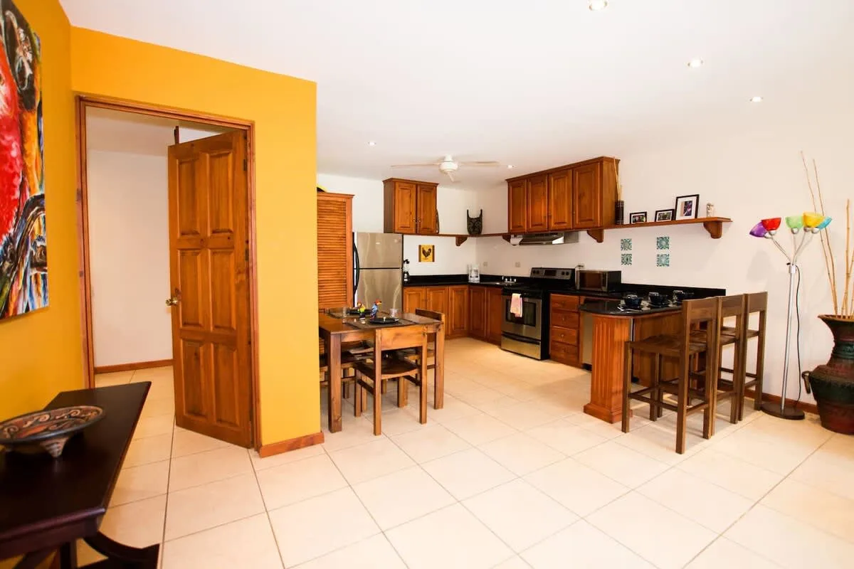 Cocina y comedor con armarios de madera, una mesa y asientos junto a la barra.