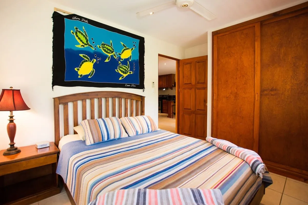 Un dormitorio con una cama a rayas debajo de un tapiz colorido de tortugas marinas.