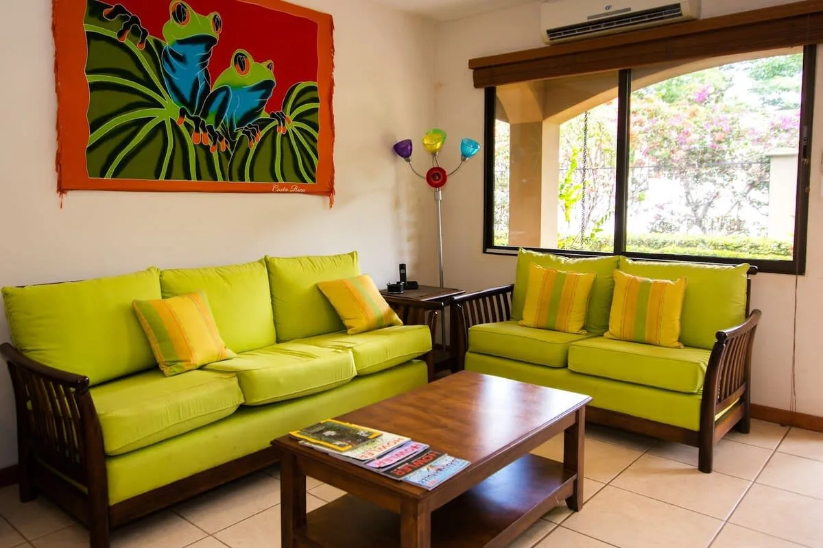 Una sala de estar con asientos verde brillante, una mesa de centro de madera y arte colorido de ranas.