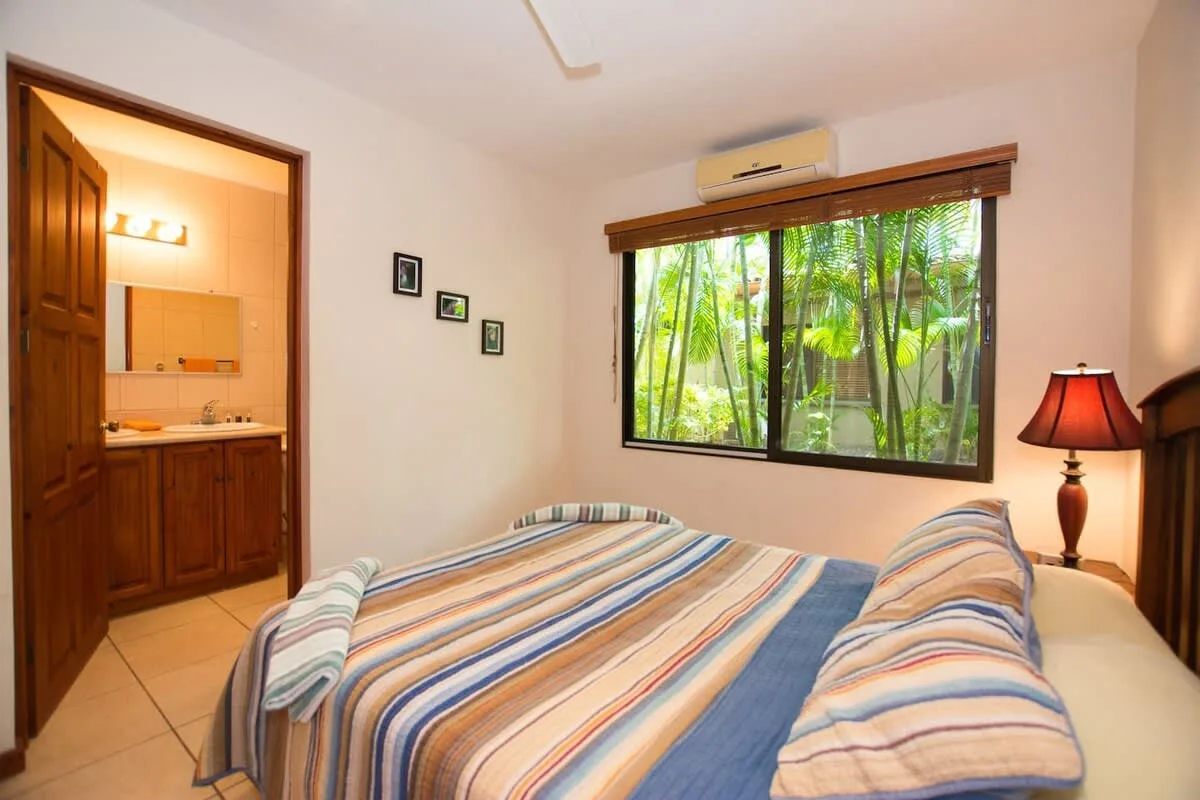 Un dormitorio con una colcha a rayas junto a una ventana con vegetación.
