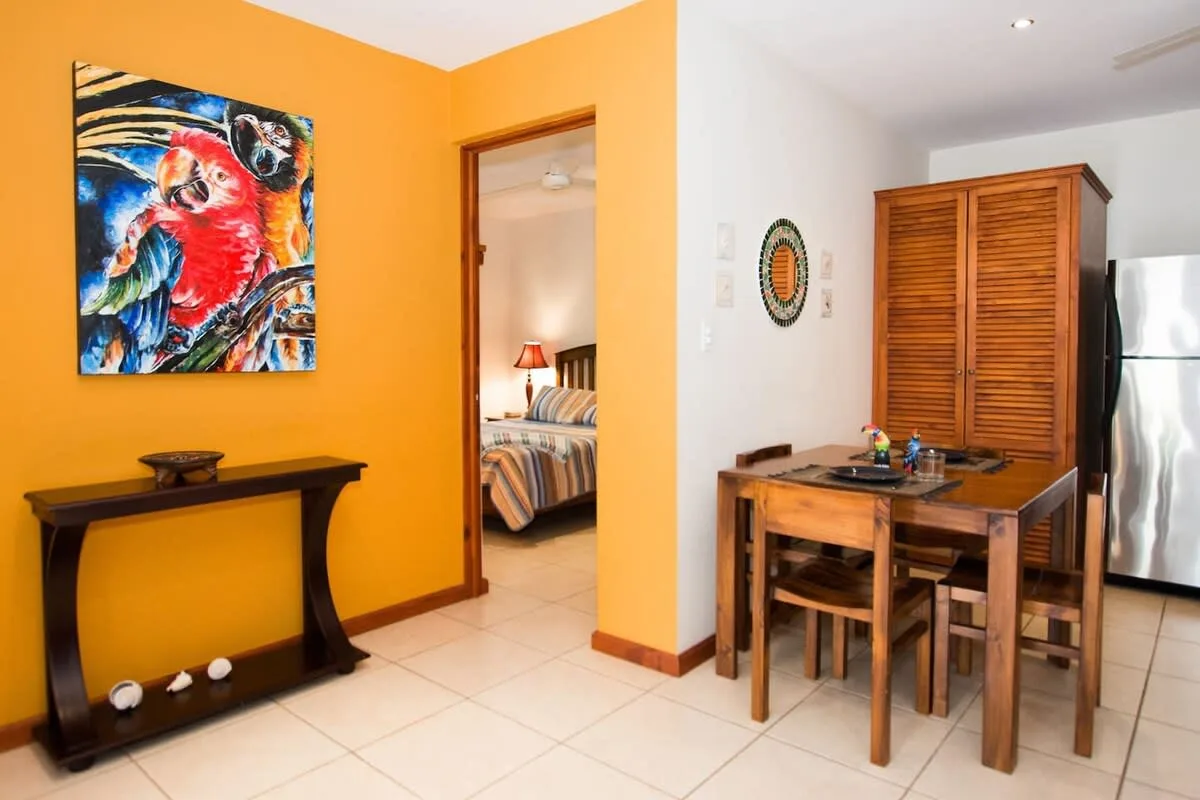 Un comedor con mesa y sillas de madera junto a un pasillo de color naranja.