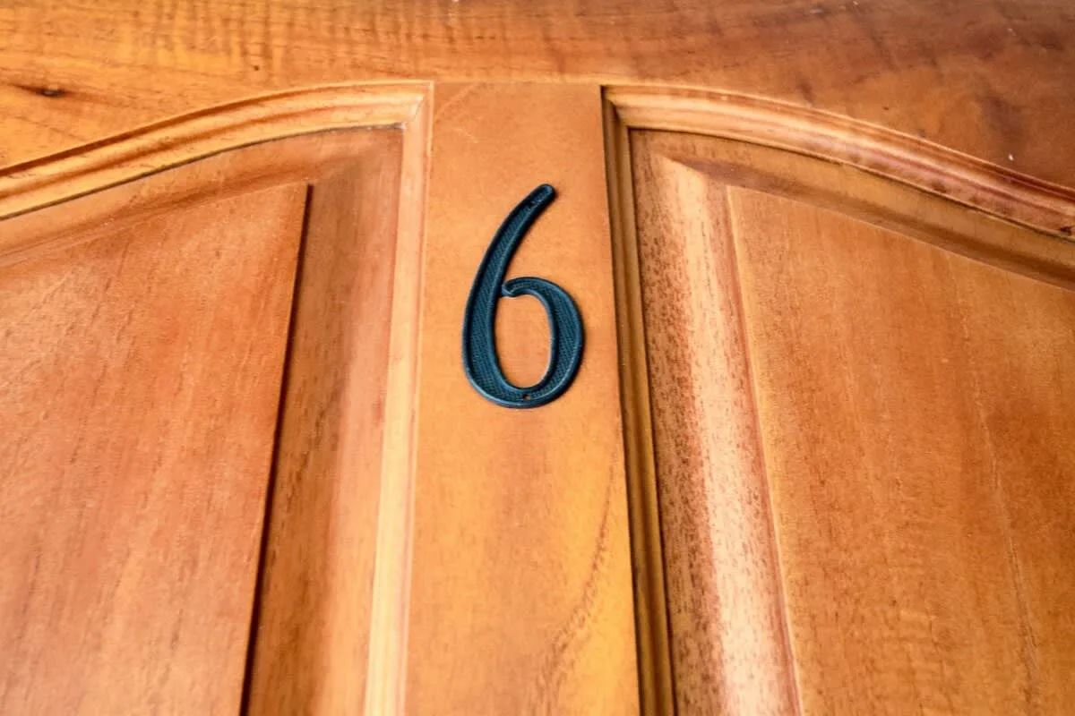 Una puerta de madera con un número seis oscuro fijado cerca del centro.