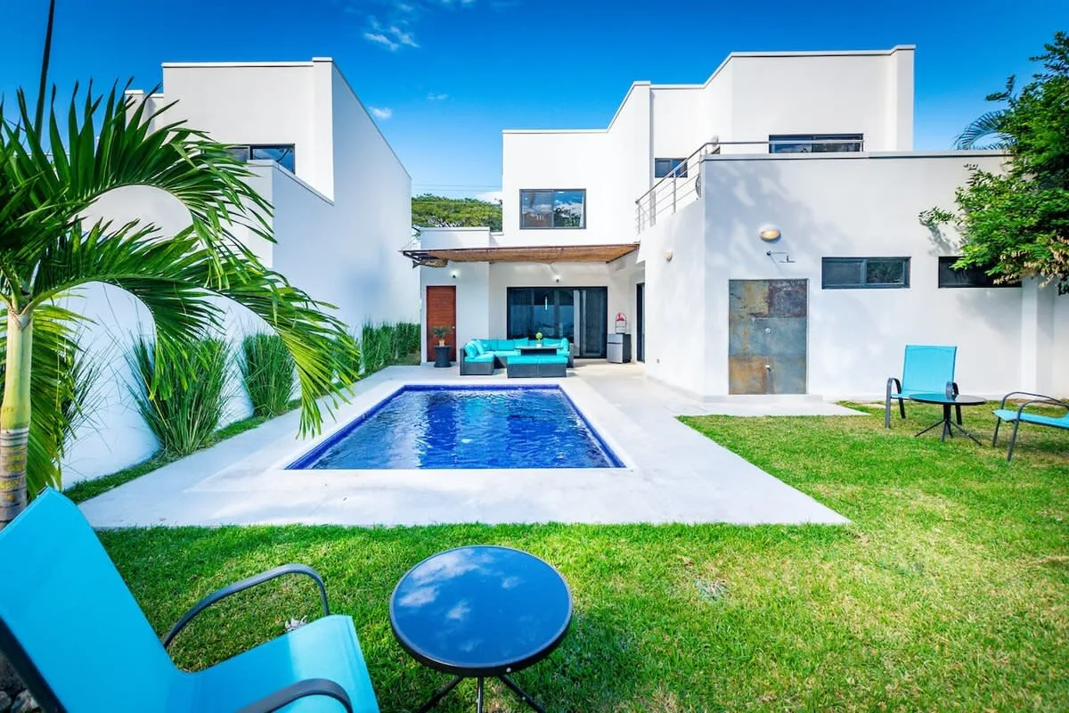A modern white house surrounds a backyard pool and lawn.