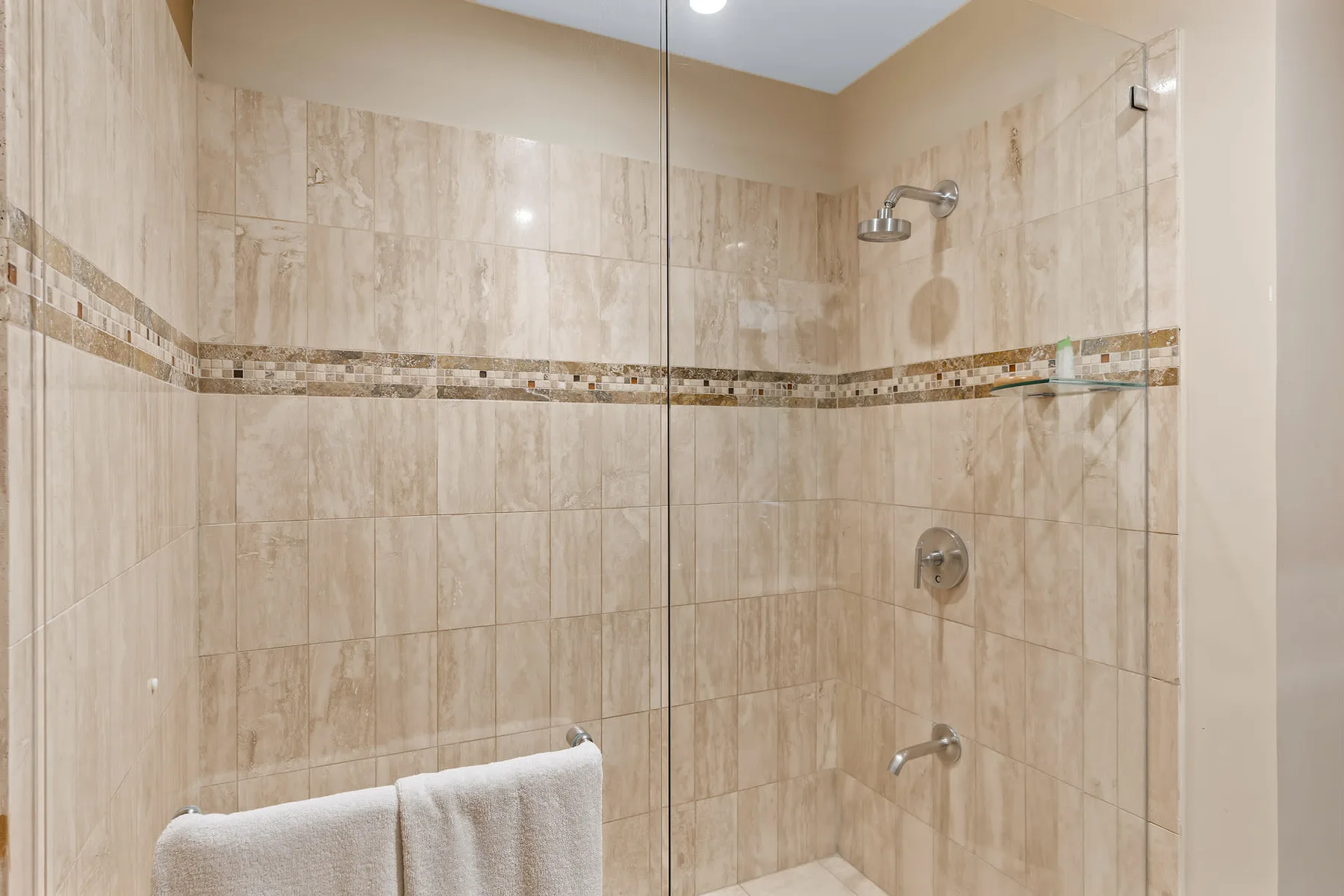 A tiled bathroom shower area with a towel hanging in the foreground.