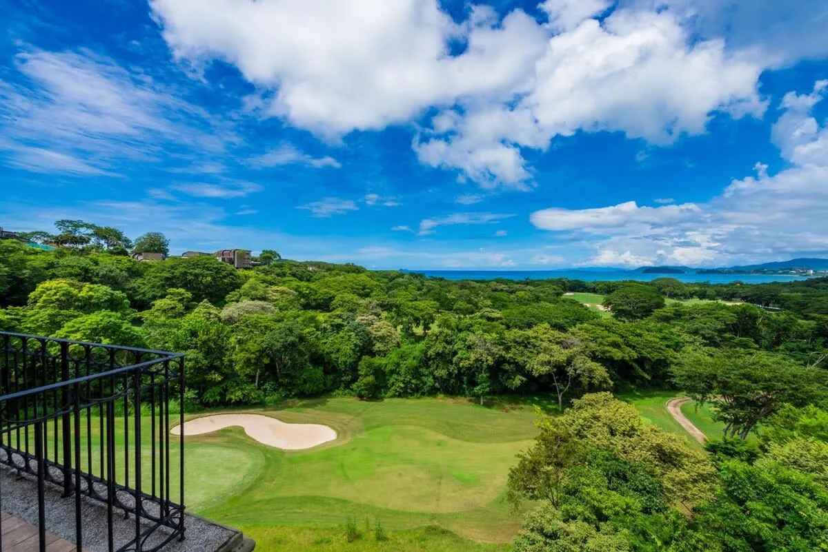 A green golf course bordered by trees beneath a partly cloudy sky.