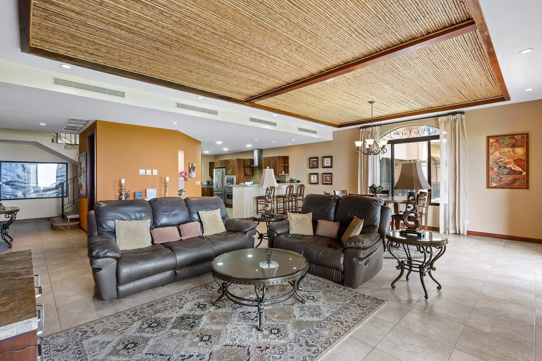 A spacious living room with dark seating, a patterned rug, and a dining area.