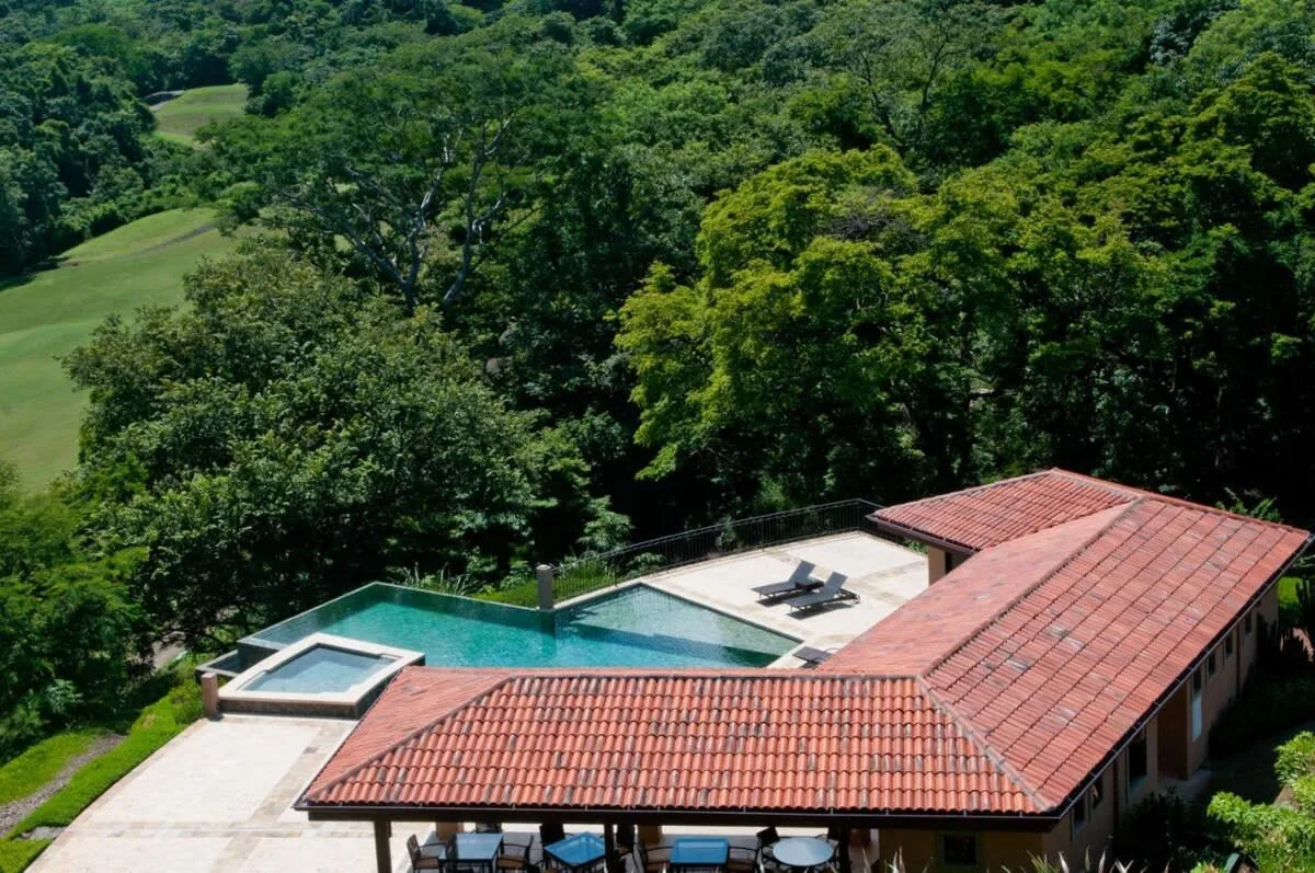 An outdoor swimming pool beside a red-tiled building, surrounded by trees.