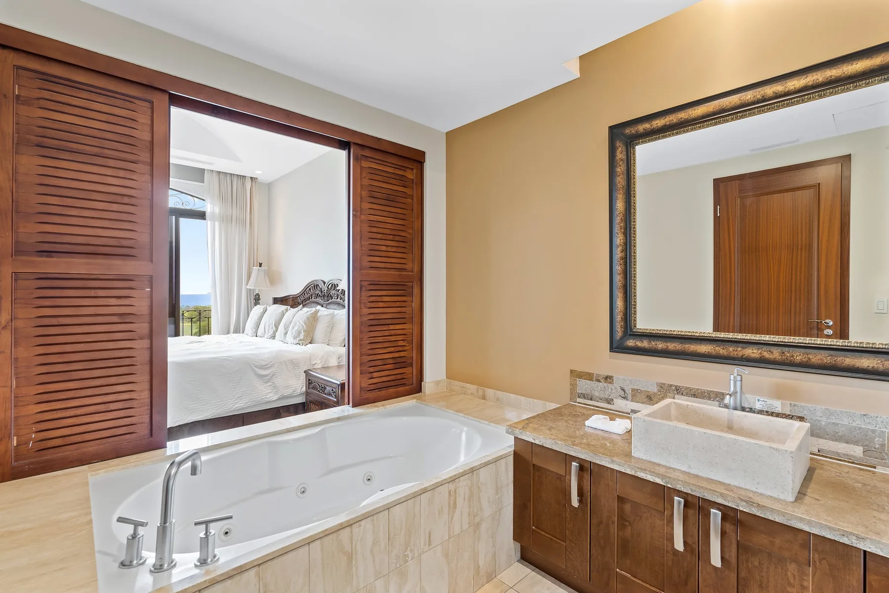 A bathroom with a bathtub, vanity, and mirror beside an open bedroom doorway.