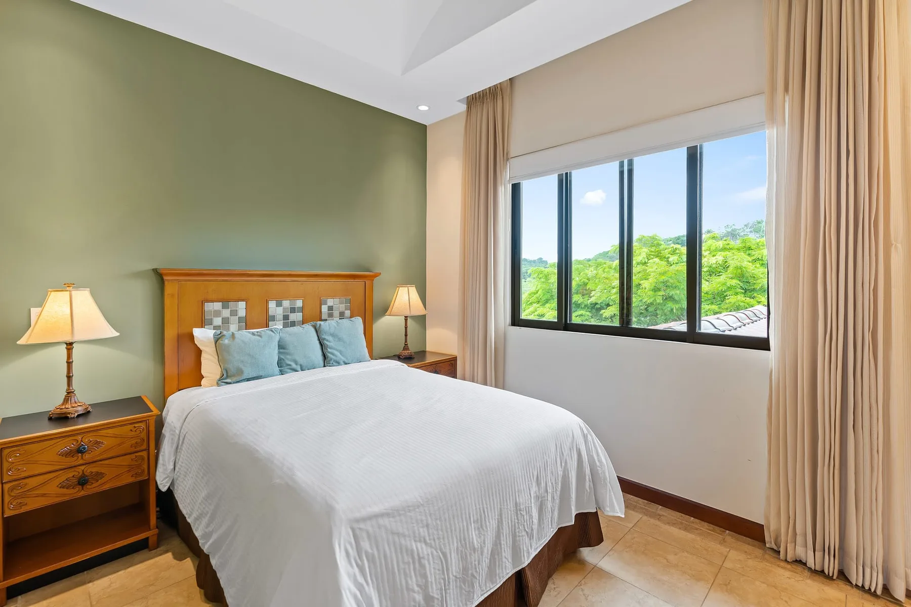 A bedroom with a neatly made bed and a large window overlooking greenery.