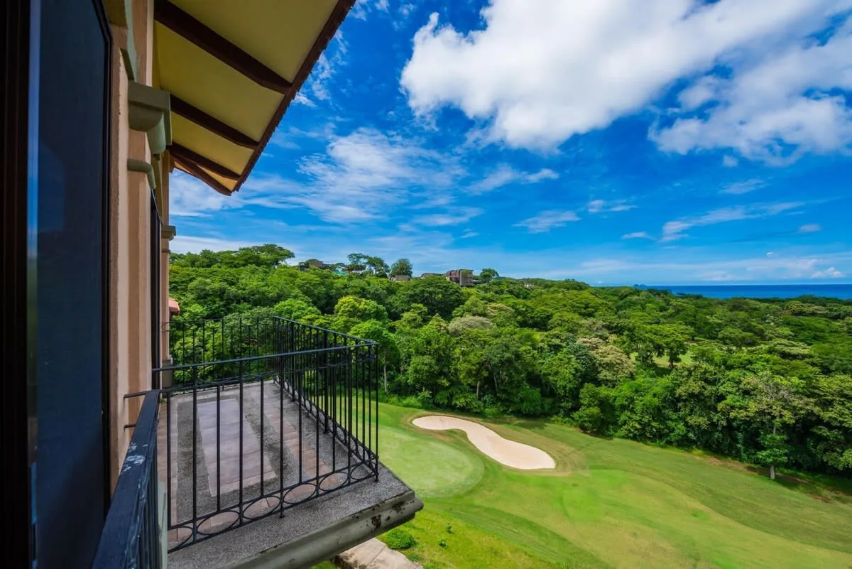 A balcony overlooks a green landscape, with the ocean visible on the horizon.