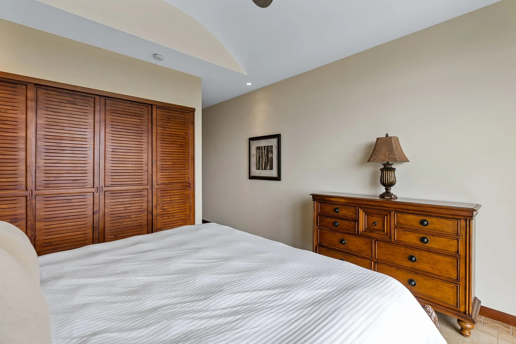 A bedroom with a bed, wooden dresser, and louvered closet doors.