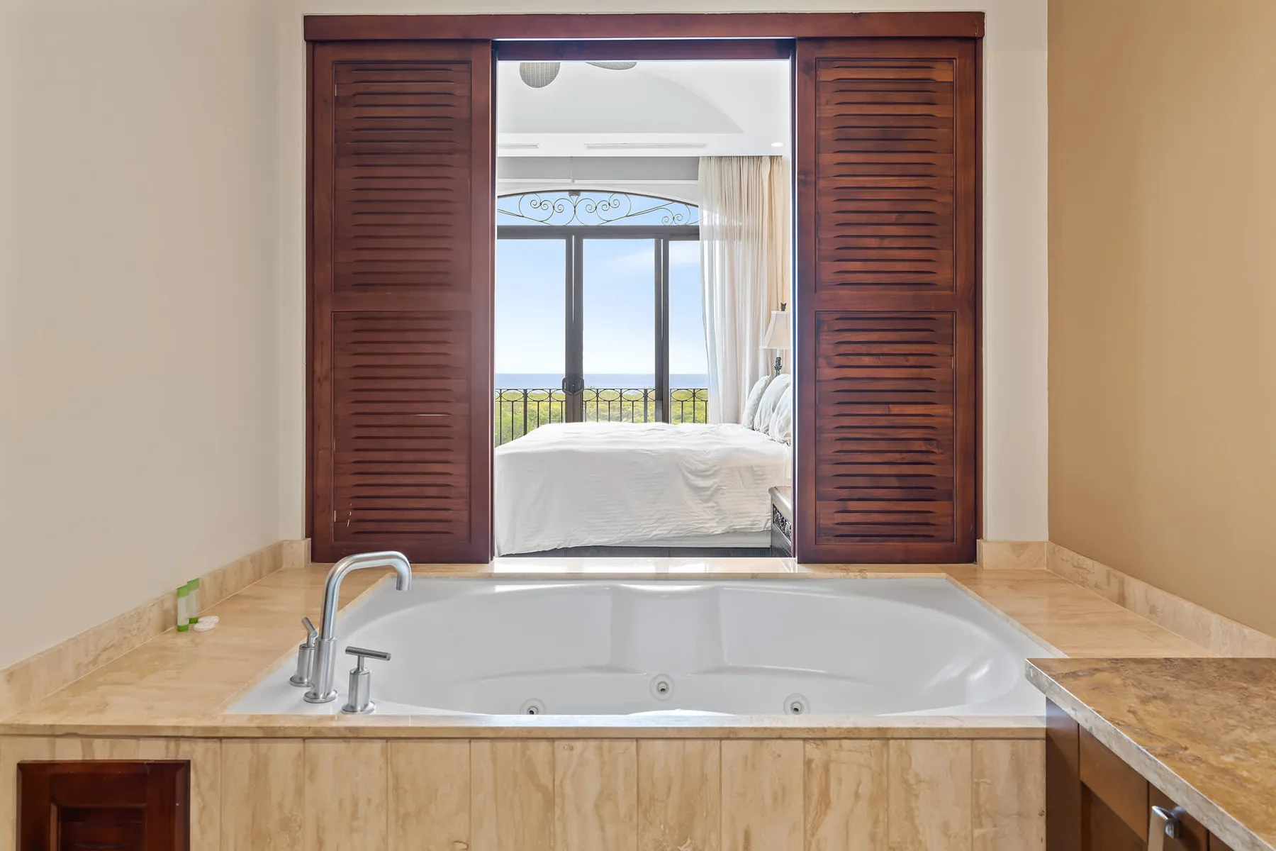 A built-in bathtub sits in the foreground, with a bedroom visible through open wooden doors.