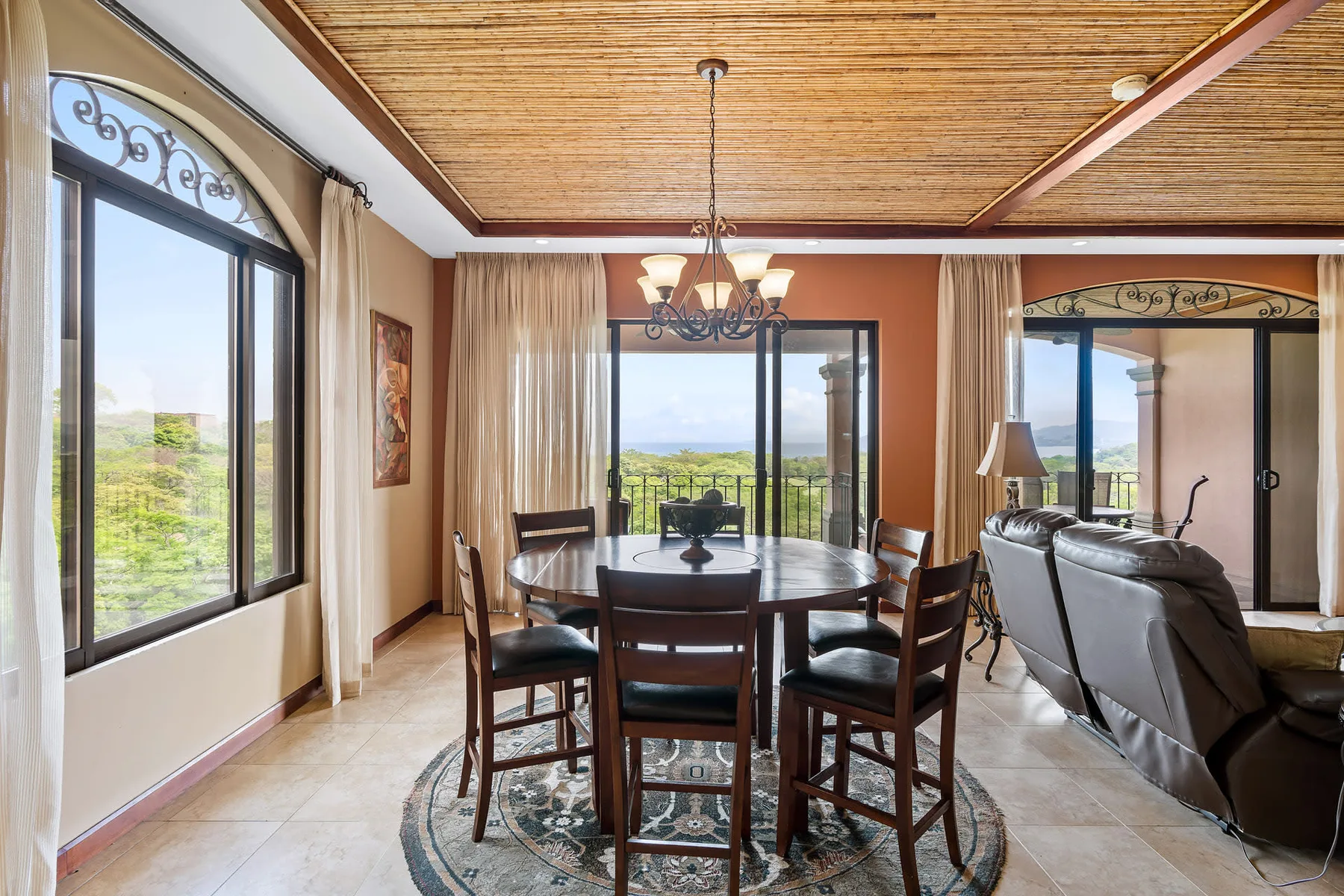 A dining area with a dark table and chairs beside large windows.