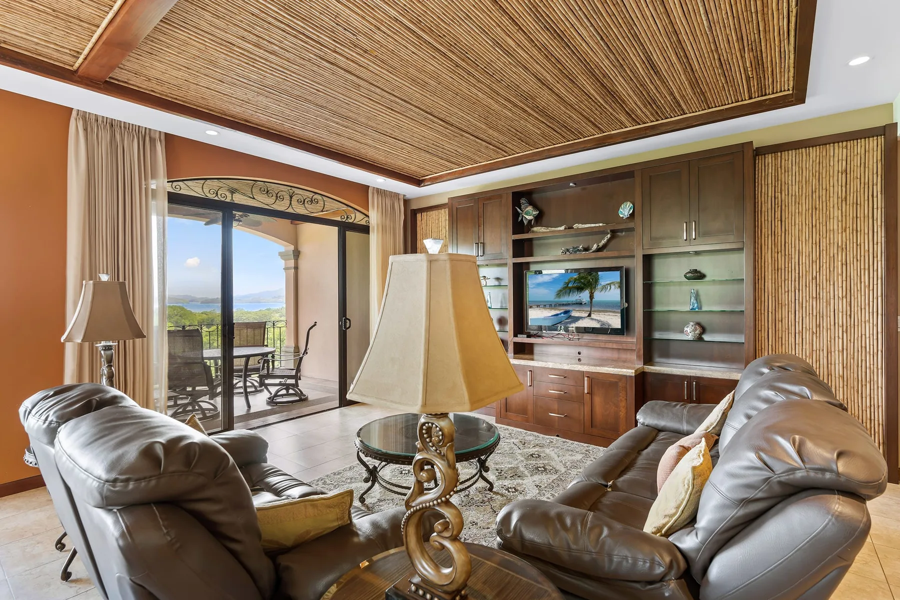 Living room with leather seating, a wooden entertainment unit, and glass doors opening onto a balcony.
